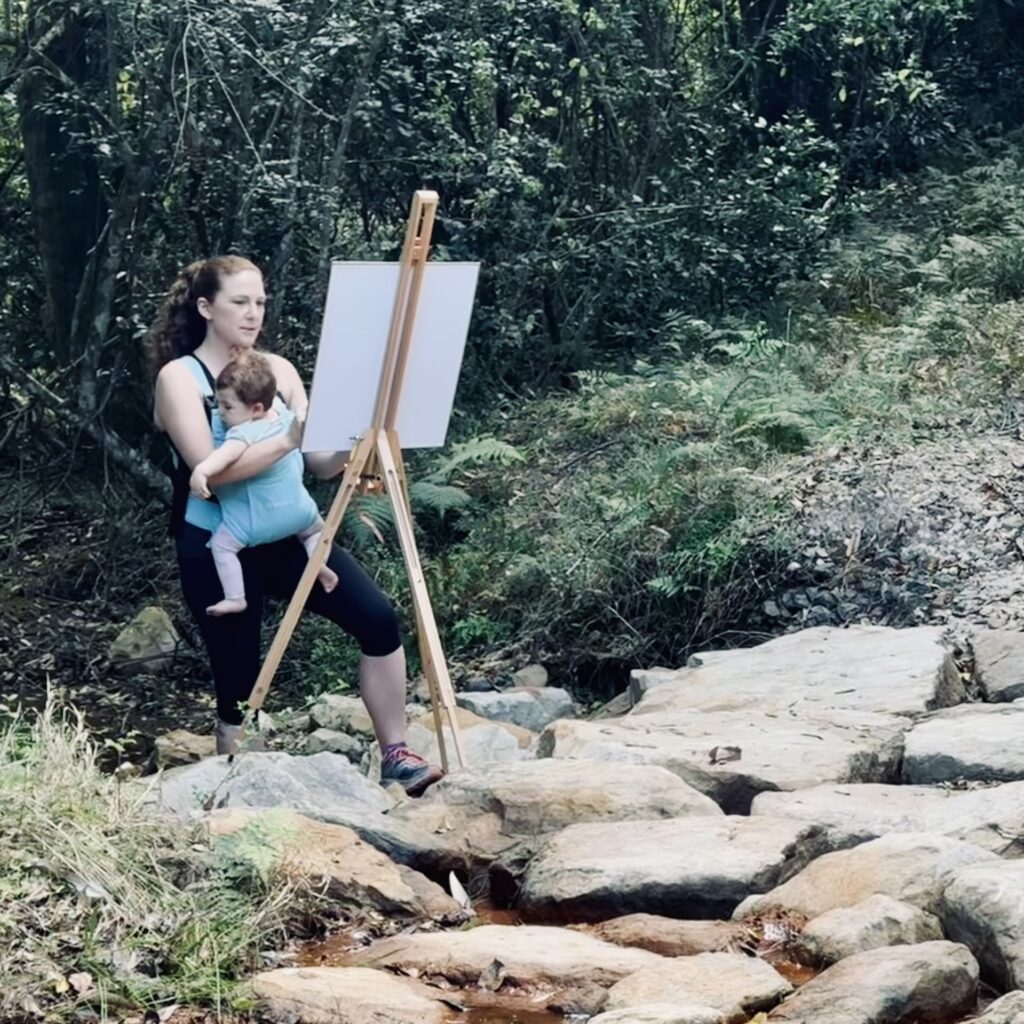 Fine Art Central Coast NSW Ruth Conwell at easel in creek with baby